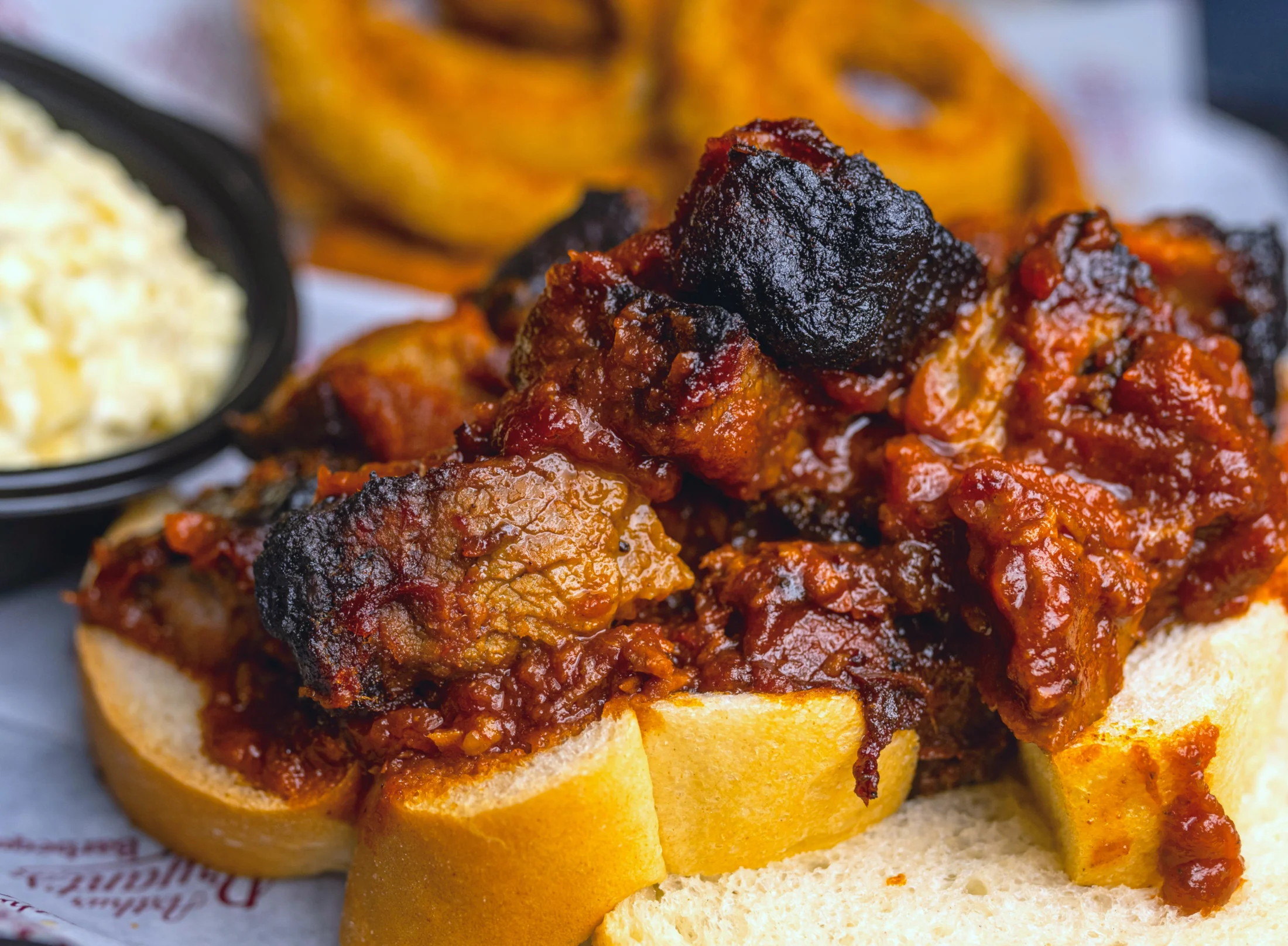 A close-up of Arthur Bryant’s sauced burnt ends on white bread, with sides in the background